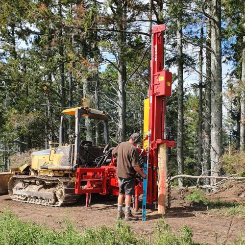 The Ultimate postdriver with 180 degree rotation on a bulldozer on a new fence line in front of trees
